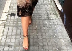 youthful female hippie is walking barefoot in public street
