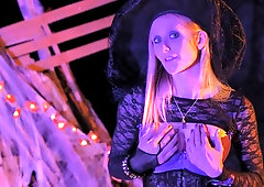 Blonde witch Kelly Dolls casts a spell under glowing Halloween lights