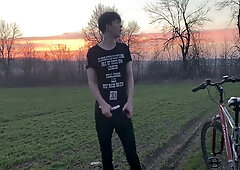 Young man with curly brown hair jerks off outdoors on a red bicycle during sunset